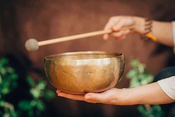 Hand holding a singing bowl with a mallet poised to strike.