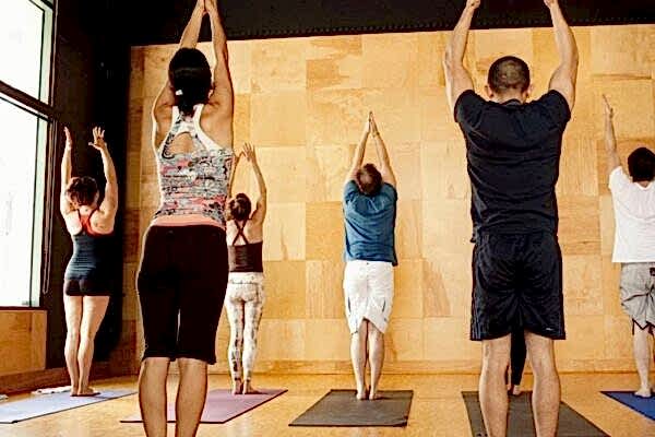 Group yoga session with participants stretching upwards on mats.
