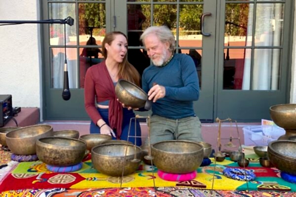 Two people examining metal bowls at an outdoor market stall.
