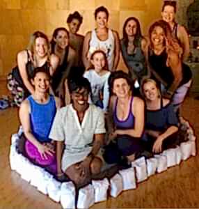 A group of people sitting and standing in a cozy indoor setting, smiling at the camera.