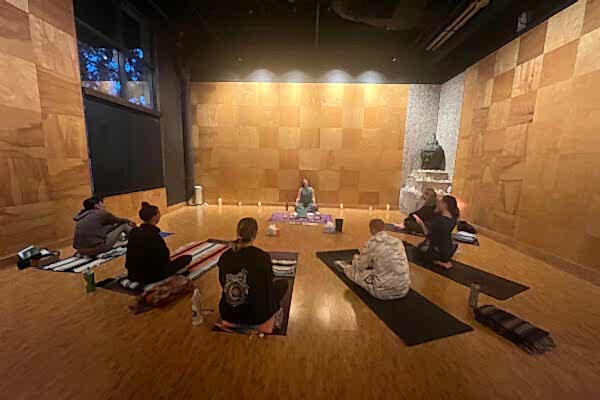 A group practicing yoga in a dimly lit studio with wooden walls and floor.