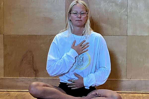 Woman meditating cross-legged indoors with hand on chest.