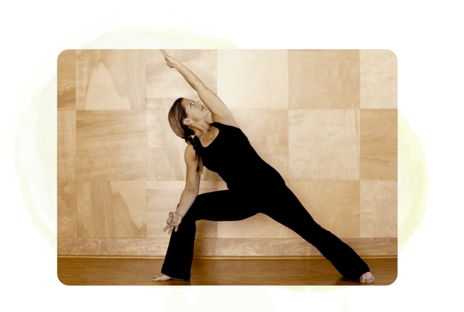 Woman practicing yoga in a black outfit against a wooden wall.