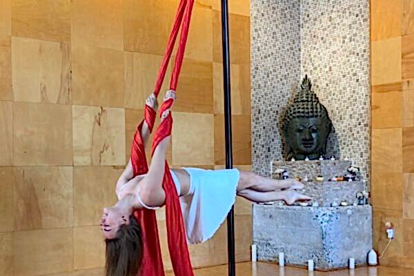 Aerial silk artist performing indoors with red fabric.