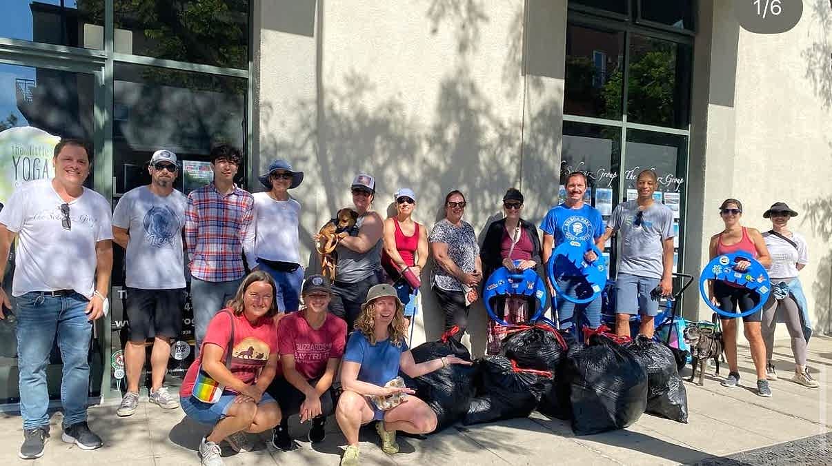 Group of people posing outdoors with trash bags during a cleanup event.